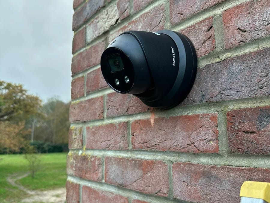 Black Hikvision turret camera on a brick corner overlooking grounds