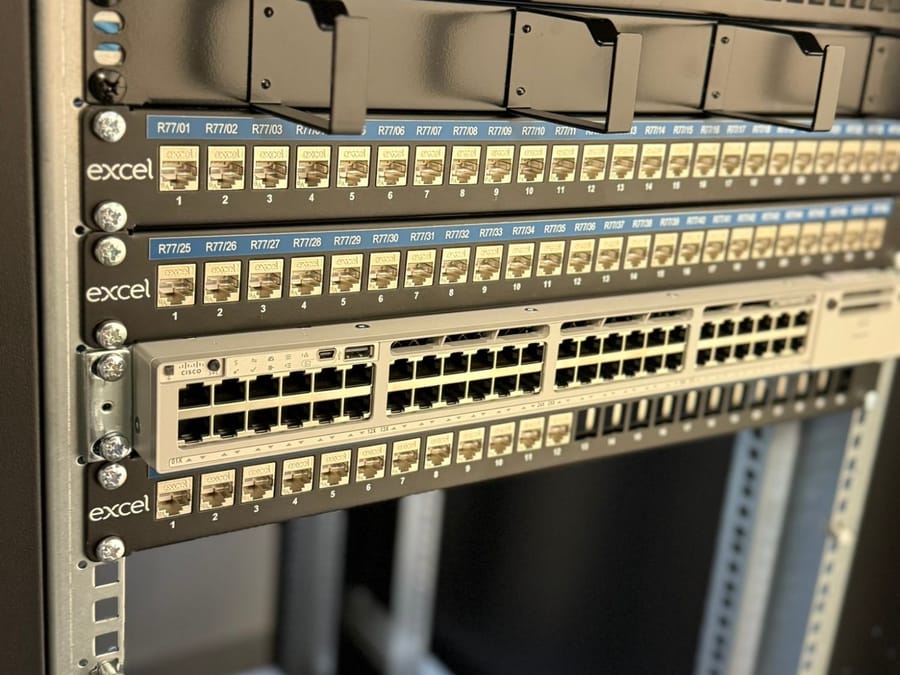 Labelled Excel Cat6A patch panels, an OM3 fibre panel and a Cisco switch in a rack